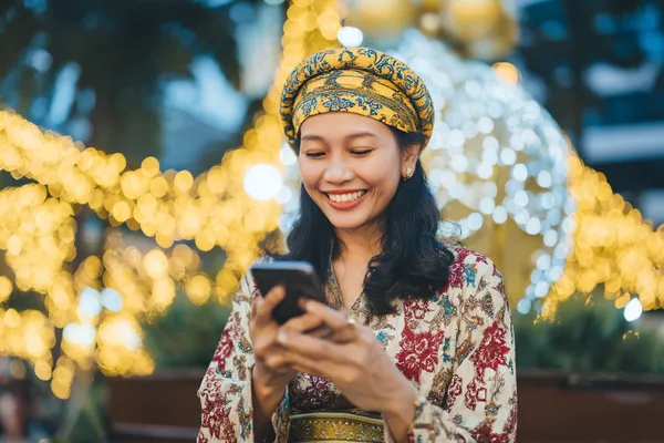 A cheerful woman in traditional clothing using her smartphone during a festive moment, showing how easily the SPINARA app fits into everyday life.