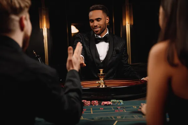 A professional dealer in a tuxedo greeting players at the roulette table, symbolizing the authentic live casino feel at SPINARA.