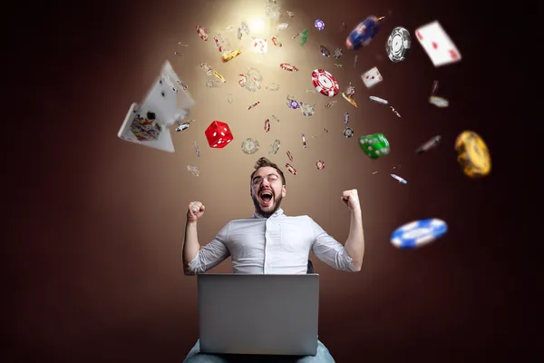 A man celebrating a winning moment on his laptop while gaming symbols float around him, capturing the excitement of SPINARA games.