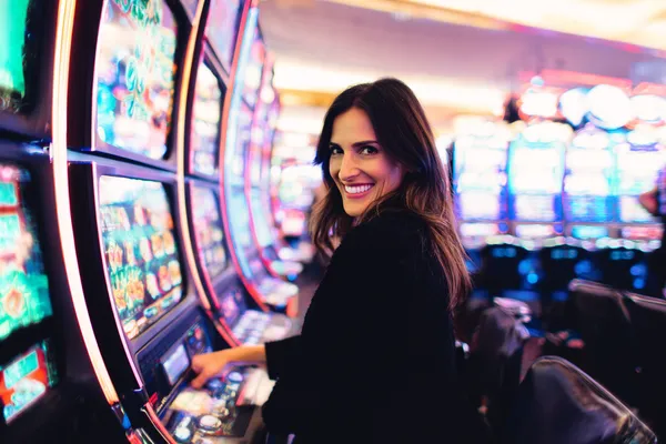 A woman smiling by bright slot machines showing lucky symbols, showcasing the exciting slot offerings at SPINARA.
